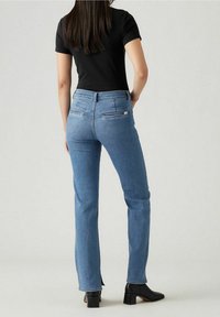 Jeans rectos de color azul claro con un diseño clásico. Presentan bolsillos traseros, trabillas para el cinturón y sutiles detalles de costura. Combinados con una blusa negra y botas.