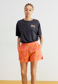 T-shirt en coton noir avec détail de logo, associé à un short à motifs vifs rose et orange, doté d'une taille élastique et d'une coupe décontractée.