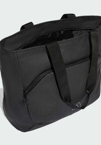 Svart vadderad tote-väska med dubbla svarta bärhandtag, med en framfickan med dragkedja. Slät textur och rektangulär form.