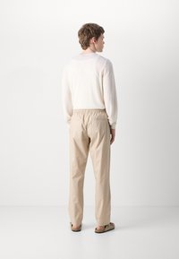 Beige bukser med elastisk talje, parret med en lysecreme langærmet top. Outfittet har en afslappet pasform og bløde teksturer.