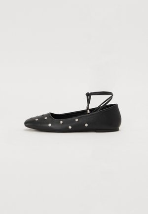 Black ballet flats made of smooth leather, featuring a pointed toe and embellished with silver studs. An ankle strap with bow detail finishes the design.