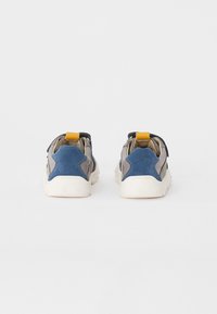 Sneaker mit einem Obermaterial aus blauem und grauem Wildleder, weißer Gummisohle und gelbem Fersenriemen. Verfügt über eine abgerundete Form und strukturierte Akzente.