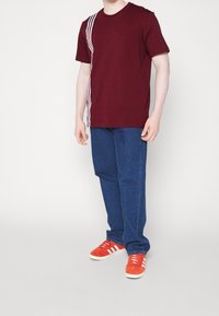 Bordó tričko s bílými pruhy na levé straně, spárované s modrými džínami a červenými teniskami s bílými pruhy. Jednoduchý, neformální design.