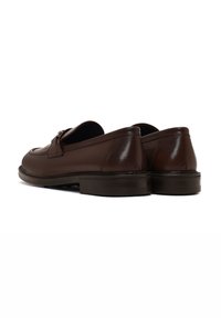 Brown leather loafers with a smooth texture, rounded toe, and a low stacked heel. Features a front buckle detail and stitching accents.