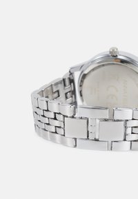 Montre en acier inoxydable argenté avec un bracelet en maille, présentant des maillons rectangulaires et une finition polie. Logo de la marque visible au dos du boîtier.