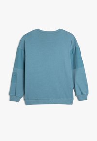 Sudadera azul con cuello redondo, mangas largas, puños y dobladillo acanalados, con una textura suave y acentos en los hombros en contraste.