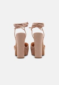 Nude high-heeled sandals with a textured suede finish, thick block heels, and crisscross ankle straps for secure fitting.