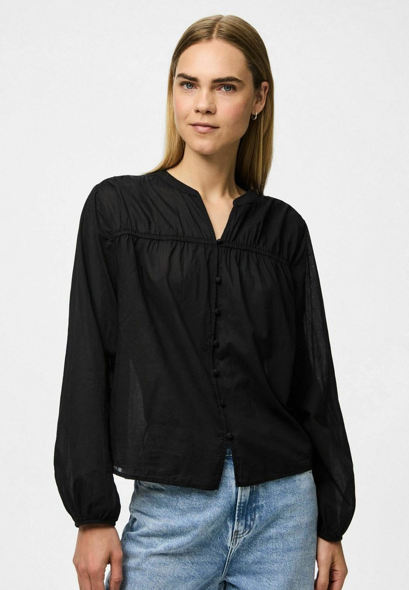 Svart långärmad blus med v-ringning och knäppning framtill, utrustad med draperade detaljer och ett lätt, något genomskinligt tyg.