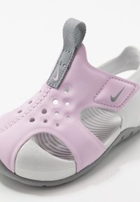 Infradito Nike rosa e bianchi con superiore in gomma testurizzata, fori di ventilazione e un gancio grigio. Presenta una suola flessibile per il comfort.