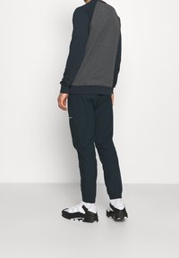 Harmaa ja laivastonsininen collegepaita, jossa pitkät hihat ja resorit hihoissa, yhdistettynä tummiin verryttelyhousuihin ja mustavalkoisiin tennareihin.