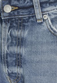 Pantalones vaqueros de mezclilla azul claro con herrajes de bronce, textura desgastada y costuras amarillas. Presenta un botón de metal y costuras de bolsillo visibles.