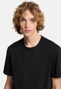 Czarna koszulka z krótkim rękawem i okrągłym dekoltem, wykonana z gładkiej bawełny, o klasycznym kroju, bez wyraźnych wzorów czy akcentów.