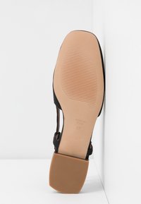 Semelle de chaussure en tissu noir avec un talon lisse beige et un dessous texturé. Présente un design découpé et une inscription "FABRIQUÉ EN ESPAGNE" avec la taille 37.