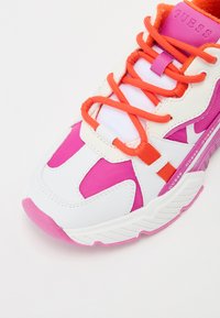 Sneaker atletico bianco e rosa con materiale testurizzato, lacci arancioni, suola pronunciata e un dettaglio con logo sul lato.