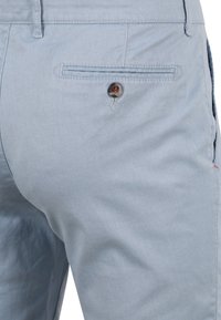 Hellblaue Chinos aus einem strukturierten Stoff, mit einer Gesäßtasche und einem braunen Knopf. Klare Linien und klassischer Schnitt.