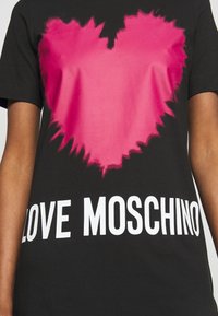 Czarny t-shirt z krótkim rękawem z gradientowym różowym sercem oraz napisem "LOVE MOSCHINO" wydrukowanym dużymi białymi literami.