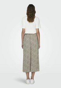 White t-shirt paired with a flowing, ankle-length skirt featuring a beige background and black speckled pattern, completed with white sneakers.