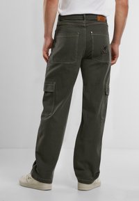 Pantalones cargo de algodón en verde oscuro, con dobles bolsillos traseros y bolsillos laterales, acabados con costuras en contraste y un parche con el logo.