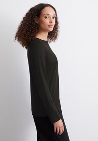 Czarny, długosleeve top wykonany z gładkiego materiału, z okrągłym dekoltem i luźnym krojem, z subtelnymi detalami przeszycia wzdłuż szwów.
