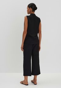 Black sleeveless top with a high neck, paired with wide-leg black pants, made from a soft fabric, featuring a smooth texture and minimal design.