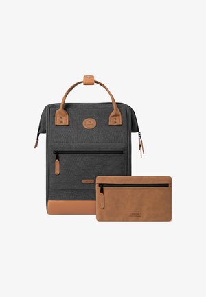 Sac à dos en tissu gris avec des accents en cuir brun, comprenant une poignée supérieure, une poche zippée à l'avant et une trousse à glissière assortie en brun.