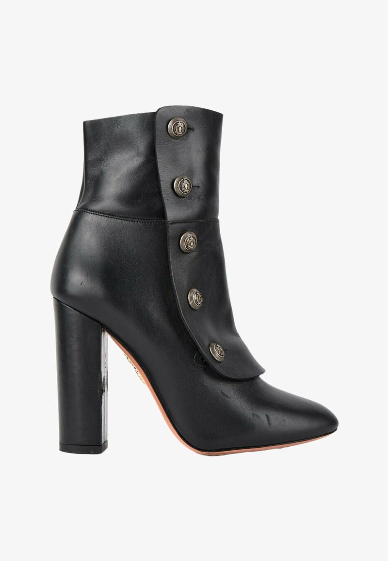 Bottine en cuir noir à talon haut avec rabat avant plié maintenu par cinq boutons métalliques décoratifs.