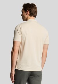 Beige polo skjorte med korte ermer og kragehals, laget av et glatt, lett stoff, med sidespalter i nederkant.