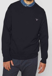 Czarna bluza z okrągłym dekoltem, długimi rękawami i małym haftowanym logo na piersi, zestawiona z spodniami w paski dla kontrastu.