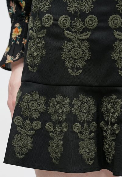 Μαύρη υφασμάτινη φούστα με περίτεχνη σκούρα πράσινη κεντητή διακόσμηση με λουλούδια, σε φαρδιά γραμμή και υφή με ανάγλυφη εμφάνιση.