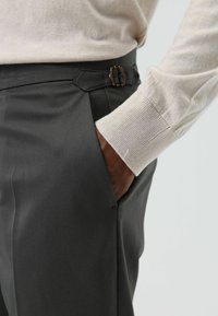 Grijze afgestemde broek met een zijzak en een verstelbare gespdetail aan de tailleband. De stof oogt glad met een matte afwerking.