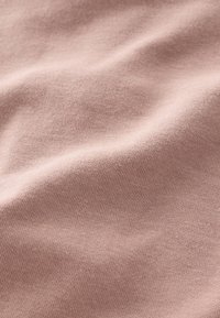 Tissu en coton rose pâle avec une texture lisse, présentant des motifs tricotés fins et subtils, légèrement froissé et drapé.