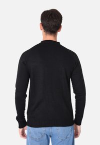Maglione nero a maglia con scollo rotondo, maniche lunghe, polsini e orlo a coste, indossato sopra jeans azzurri chiari.