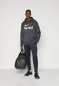 Gray Nike hoodie with a large white logo, paired with black Nike pants and shoes. The individual holds a black duffel bag.