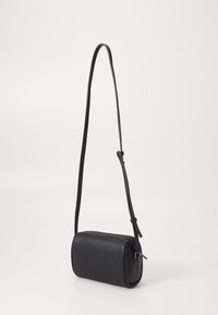 Sac bandoulière noir avec une surface texturée, forme cylindrique, sangle ajustable fine et fermeture zippée. Des accents lisses améliorent son design.
