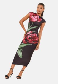 Čierne kvetinové šaty s veľkými červenými kvetmi a zelenými listami. Hladká tkanina, priliehavý strih, krátke rukávy a detail na bokoch s nariasením.