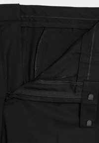 Czarne spodnie z gładką fakturą, zapinane na zamek błyskawiczny, z guziczkami jako akcentami. Wnętrze podszyte miękkim materiałem, z detalami w postaci przeszyć.