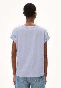 Lilac short-sleeve T-shirt with rolled cuffs, round neckline, and a relaxed fit, paired with light blue denim jeans. Smooth cotton texture.