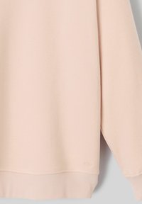 Sweat-shirt rose clair avec une finition douce et texturée, des poignets et un ourlet côtelés, et un petit logo sur le bas.