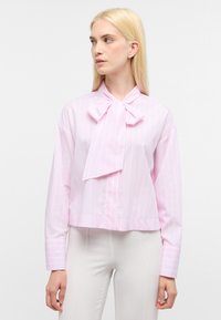Blusa a strisce rosa chiaro con colletto a fiocco e maniche lunghe, realizzata in un tessuto morbido. Lunghezza cropped con chiusura a bottoni sul davanti.