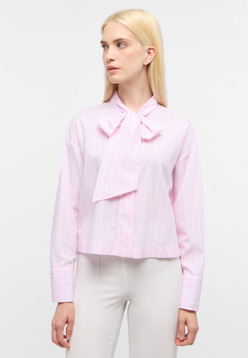 Blusa a strisce rosa chiaro con colletto a fiocco e maniche lunghe, realizzata in un tessuto morbido. Lunghezza cropped con chiusura a bottoni sul davanti.