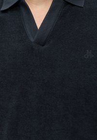 Gros plan d'une chemise bleu marine à col avec col en V et tissu subtilement texturé montrant partiellement le cou et la poitrine.