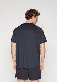 Camiseta deportiva negra de cuello redondo y mangas cortas, con un tejido texturizado y un dobladillo trasero más largo para mayor cobertura.