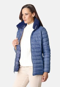 Chaqueta de plumas azul con cierre de cremallera, textura acanalada y un cuello mullido, que cuenta con un forro estampado en tonos azules más claros.