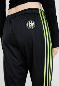 Melnas sporta bikses ar zaļām svītrām gar malām un apaļu logo uzlīmi ar numuru 13 aizmugurē. Gluda tekstūra.