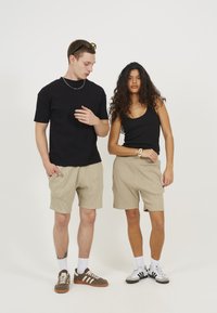T-shirt noir à manches courtes et short rayé beige sur un modèle masculin. Modèle féminin en débardeur noir et short beige, portant une montre.