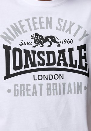 Bijela pamučna majica s velikim crno-sivim grafičkim printom. Tekst uključuje "Lonsdale", "Devetnaest Šezdeset" i ilustraciju lava.