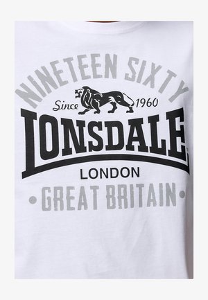 Tricou alb din bumbac cu un imprimeu grafic mare în culori negru și gri. Textul include "Lonsdale," "Nineteen Sixty," și o ilustrație cu un leu.