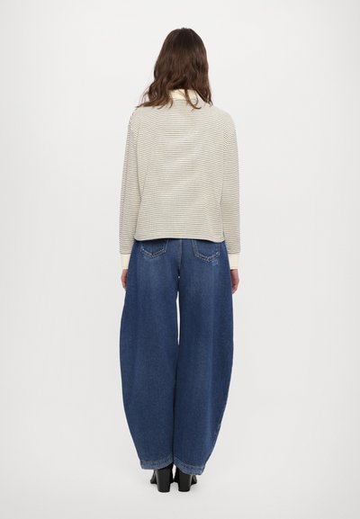 Maglione a righe, crema e nero con colletto alto; abbinato a jeans a gamba larga, blu scuro. Il maglione presenta polsini a coste; i jeans hanno tasche posteriori.