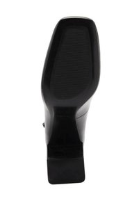 Schwarze hochhackige Schuhsohle mit strukturiertem Grip-Muster, geschwungener Form und Klettverschlussakzent auf der Rückseite, aus synthetischem Material gefertigt.