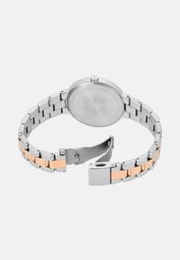 Hõbe roostevabast terasest kellarihm roosakuldsete aksessuaaridega, ümmarguse korpuse ja kokkuklapitava pandlaga. Tagaküljel on brändi graveering.